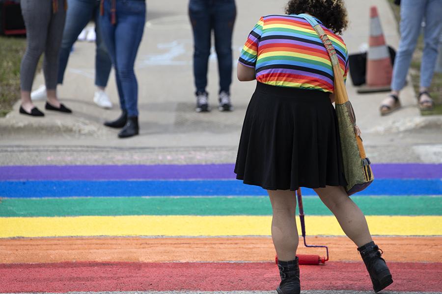 一个穿着彩虹衬衫的人帮助把道路涂成彩虹色.
