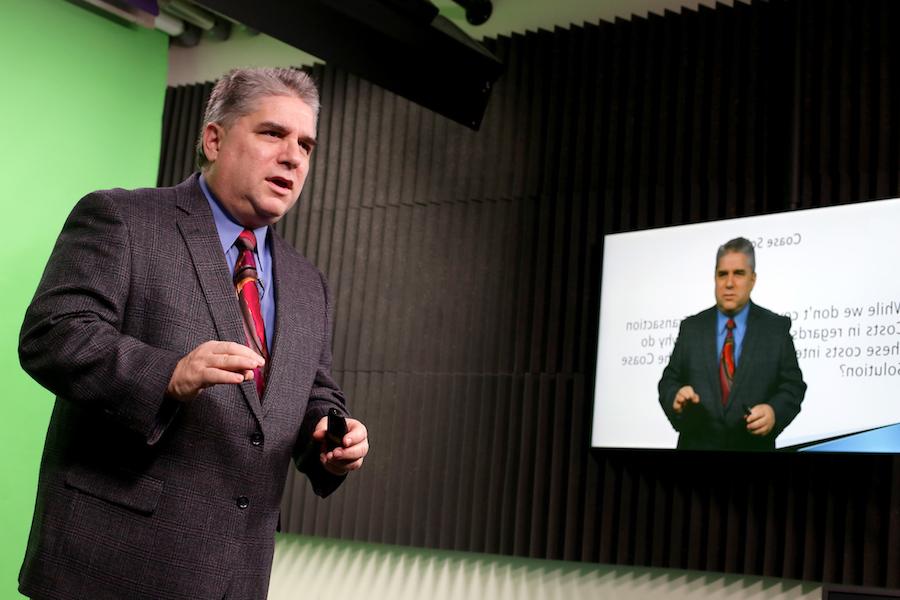 Image: Professor standing in front of a gren screen super imposed onto a powerpoint slide.